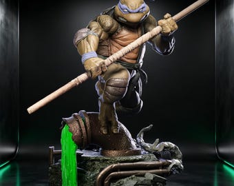 May include: A detailed figurine of a muscular anthropomorphic turtle character wearing a purple mask and wristbands, holding a wooden bo staff. The figure stands on a base featuring a rusted pipe leaking bright green slime onto rocky debris.