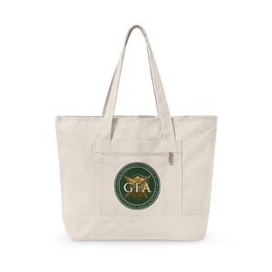 May include: A cream-colored canvas tote bag with two shoulder straps and a front zippered pocket. The pocket features a circular green logo with the text "GRISHAM FRANCESCOCHINA ATTORNEYS AT LAW" and "CONSTITUTIONAL RIGHTS & DEFENSE" surrounding a gold shield with the letters "GFA".