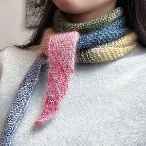 May include: A hand-knitted scarf in shades of pink, blue, green, and yellow. The scarf is wrapped around the neck, with the ends hanging down. The yarn has a textured appearance, and the colors blend together in a gradient effect. The scarf appears soft and warm.