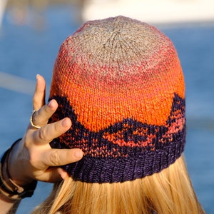 May include: A knitted hat with a gradient of colours from grey to orange to purple. The hat has a textured pattern and a wide brim.