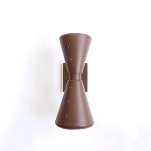 Puede incluir: Una lámpara de pared marrón con dos pantallas en forma de cono. Las pantallas tienen un patrón perforado y están unidas a una base cuadrada de metal.