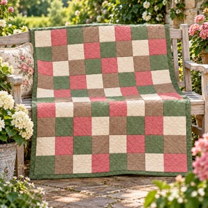 Può includere: Una trapunta patchwork rettangolare caratterizzata da un motivo a griglia ripetuto di blocchi di tessuto quadrati in colori alternati verde salvia, rosa antico, marrone chiaro e crema, rifinita con un bordo in tessuto verde salvia e cuciture.