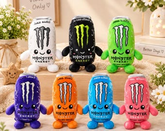 May include: A collection of seven plush toys shaped like Monster Energy drink cans in white, black, green, purple, orange, blue, and pink. Each soft toy features the iconic claw logo, a smiling face with black eyes, small arms, and feet.