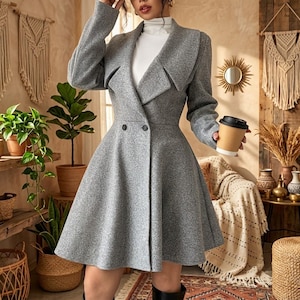 May include: A grey long-sleeved coat with a wide collar, a flared skirt, and two black buttons at the waist. The coat is worn over a white high-neck top. The fabric has a textured, heathered appearance with a structured fit through the bodice.