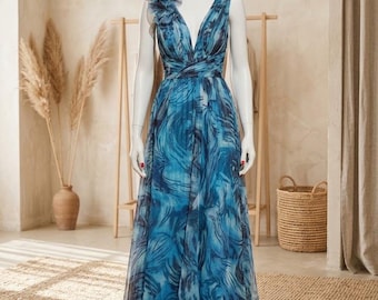 May include: A floor-length sleeveless dress in shades of blue and dark navy with a swirling abstract pattern. The bodice features a deep V-neckline, a gathered waist, and a large, sheer, ruffled floral accent on the right shoulder strap.