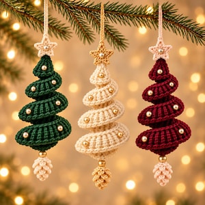Op de afbeelding: Drie spiraalvormige gehaakte kerstboomhangers in donkergroen, crème en dieprood. Elke boom heeft een gehaakte ster als piek met een centrale kraal, kleine parelachtige kralen langs de spiraalvormige takken en een gehaakte dennenappel aan de onderkant.