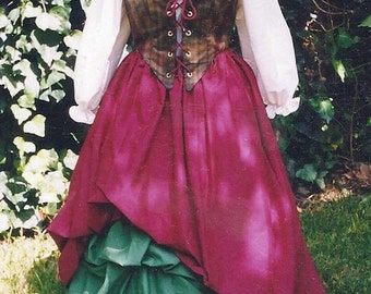 May include: A Renaissance-style costume on a mannequin. The outfit features a white blouse with ruffled neckline and sleeves, a brown plaid bodice with red lacing, and a layered skirt in shades of burgundy, green, and white. The costume is displayed on green grass.