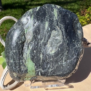May include: A large, polished, rounded stone featuring a marbled pattern of deep black and forest green mineral veins. The surface has a smooth, reflective texture with visible natural fissures and color variations throughout the rock's structure.