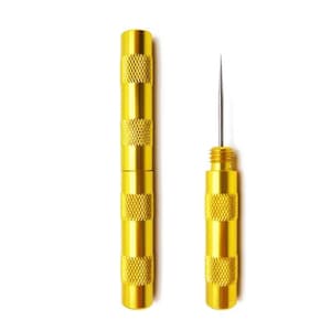 May include: A gold-colored metal tool consisting of two cylindrical parts. One part is a hollow tube with a knurled grip, and the other is a handle with a thin, sharp metal needle protruding from the top, also featuring a knurled grip.