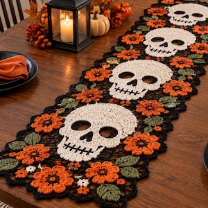 Peut inclure: Un chemin de table rectangulaire en crochet présentant un motif répétitif de quatre crânes blanc cassé entremêlés de fleurs orange vif et de feuilles vertes, le tout bordé d'une délicate bordure en crochet noir.