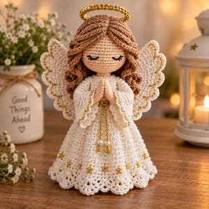 May include: A crocheted angel figurine with light brown yarn hair, a gold halo, and white wings with gold trim. The angel wears a white dress featuring gold star accents and a gold cord belt, with hands clasped in a prayer position.