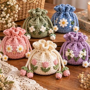 May include: Five small, round, crocheted drawstring pouches in pink, sage green, blue, cream, and lavender. Each pouch features floral appliques, including daisies and tulips, with matching crocheted flower charms attached to the drawstring ends.