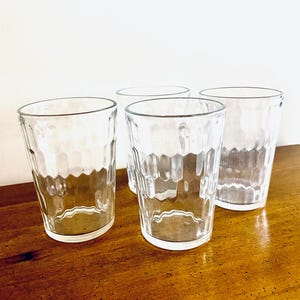 Puede incluir: Cuatro vasos transparentes con un patrón texturizado en forma de panal. Los vasos están vacíos y se encuentran sobre una superficie de madera. Los vasos son de diferentes alturas y están diseñados para bebidas.