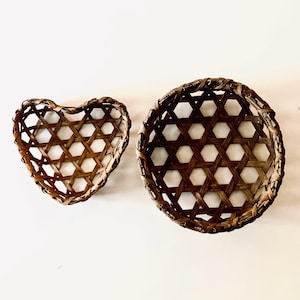 May include: Two brown woven baskets made of thin strips of wood. One basket is heart-shaped and the other is circular. Both baskets feature an open hexagonal lattice pattern throughout their structure, creating a lightweight and airy appearance.