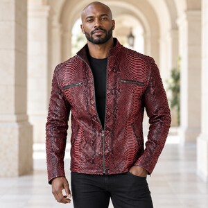 Peut inclure: Une veste &agrave; motif peau de serpent rouge fonc&eacute; et noir avec un col montant, une fermeture &eacute;clair frontale int&eacute;grale et deux poches de poitrine horizontales zipp&eacute;es. La veste est port&eacute;e sur un t-shirt noir avec un pantalon noir.