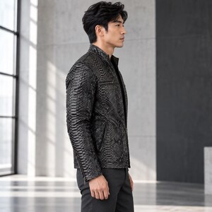 Peut inclure: Une veste noire avec un motif textur&eacute; en peau de serpent, dot&eacute;e d'un col montant, d'une fermeture &eacute;clair frontale et de poches zipp&eacute;es sur la poitrine et les c&ocirc;t&eacute;s. Le v&ecirc;tement est port&eacute; avec un pantalon noir uni, ajust&eacute;.