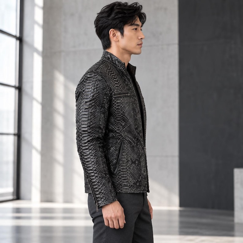 Peut inclure: Une veste noire avec un motif textur&eacute; en peau de serpent, dot&eacute;e d'un col montant, d'une fermeture &eacute;clair frontale et de poches zipp&eacute;es sur la poitrine et les c&ocirc;t&eacute;s. Le v&ecirc;tement est port&eacute; avec un pantalon noir uni, ajust&eacute;.