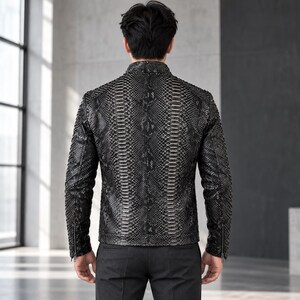 Peut inclure: Une veste noire et grise pr&eacute;sentant un motif d&eacute;taill&eacute; en peau de serpent sur tout l'ext&eacute;rieur. La veste poss&egrave;de un col montant, des manches longues avec des poignets zipp&eacute;s et une coupe ajust&eacute;e, vue de dos sur une personne.
