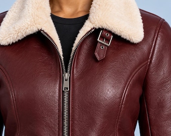 Chaqueta de aviador de cuero burdeos entallada para mujer con forro de piel sintética color crema.