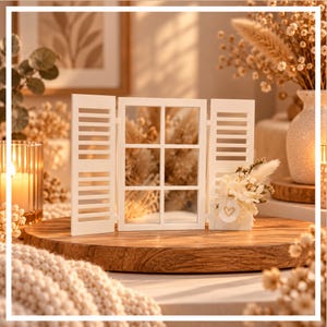 May include: A white wooden window frame decoration with two hinged shutters. The right shutter is adorned with a small arrangement of dried flowers and a white circular tag featuring a gold heart outline in the center.