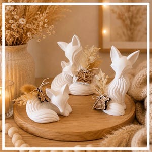 Può includere: Tre statuette di volpe bianche dalle linee lisce e curve, ciascuna decorata con piccole composizioni di fiori secchi e un'etichetta in legno con il testo tagliato al laser Herbst Zauber, disposte su un vassoio rotondo in legno.
