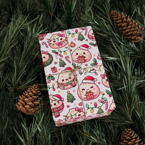 Könnte beinhalten: Eine rechteckige Geschenkbox, eingewickelt in weißes Papier mit einem wiederkehrenden Muster aus Cartoon-Teigtaschen, die Weihnachtsmützen und Schals tragen, durchsetzt mit Weihnachtsbäumen, Zuckerstangen, bunten Lichterketten und kleinen rosa Herzen.