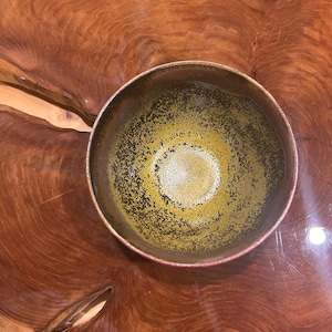 Peut inclure: Un bol en céramique rond présentant un intérieur tacheté avec un dégradé de tons brun foncé et vert olive. Le bord est lisse et circulaire, tandis que la surface intérieure affiche un motif d'émail texturé et moucheté partant du centre.