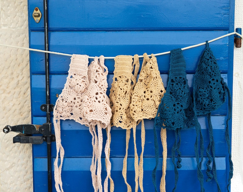 May include: Four crocheted tops hanging on a blue wooden door. Two are beige, one is light pink, and one is teal.