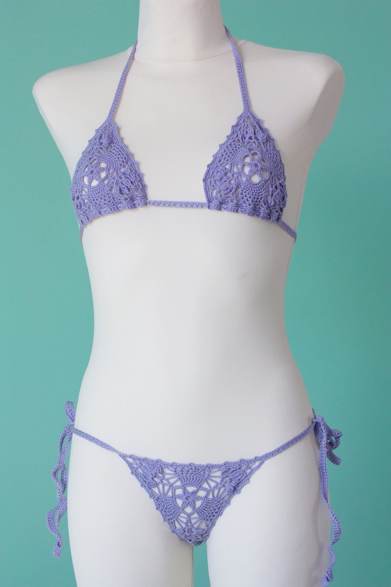 May include: A lavender crochet bikini top and bottom with a delicate floral pattern. The bikini top has adjustable straps and the bottom has ties on the sides.