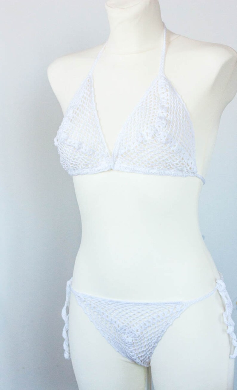 K&ouml;nnte beinhalten: Wei&szlig;er Bikini aus H&auml;kelspitze mit zartem Blumenmuster. Das Oberteil ist im Halstert-Stil mit verstellbaren Tr&auml;gern. Das Unterteil ist im Low-Rise-Stil mit B&auml;ndern an den Seiten.
