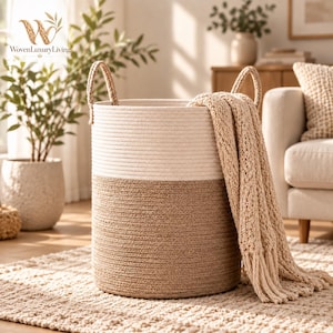 May include: A cylindrical storage basket made of coiled rope, featuring a two-tone design with an off-white upper section and a tan lower section. The basket includes two integrated rope handles and a beige knit throw blanket draped over one side.