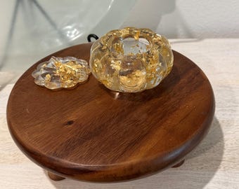 Puede incluir: Un recipiente de resina transparente con forma de calabaza y láminas de pan de oro incrustadas. El objeto cuenta con una base y una tapa extraíble de borde festoneado, ambos con un acabado translúcido y detalles dorados.