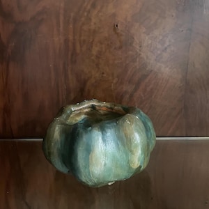 Op de afbeelding: Een kleine, ronde, komvormige keramische schaal met een geschulpte, pompoenachtige rand. De buitenkant is met de hand beschilderd met gemengde tinten diep bosgroen, gedempt olijfgroen en aardse bruintinten voor een getextureerd uiterlijk.