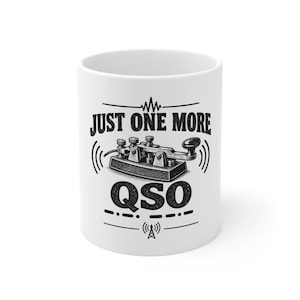 Può includere: Una tazza in ceramica bianca con un'illustrazione grafica nera di un tasto telegrafico centrata tra il testo "JUST ONE MORE" sopra e "QSO" sotto. Il design include simboli di onde radio e una piccola icona di torre radio in basso.