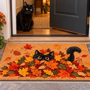 May include: A rectangular coir doormat featuring a printed illustration of a black cat peeking out from a large pile of vibrant autumn maple leaves in shades of orange, red, yellow, and green, with its fluffy tail visible on the right side.