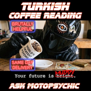 May include: A black motorcycle helmet with an eye graphic, worn by someone in black leather gloves holding a white mug with the text "WORLD'S OKAYEST PSYCHIC" containing coffee grounds. Tarot cards and a metal lighter sit on the wooden table.