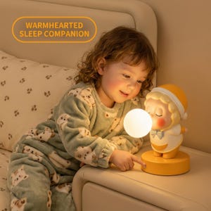 May include: A yellow and white character-shaped night light with a glowing spherical bulb. The base is yellow, and the figure features a yellow hat, a white shirt with a blue bow tie, and a round face. The text WARMHEARTED SLEEP COMPANION is visible.