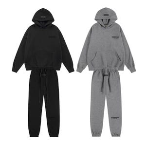 Könnte beinhalten: Zwei passende Sets aus Kapuzenpullovern und Jogginghosen in Schwarz und Anthrazitgrau. Jeder Kapuzenpullover hat eine Kängurutasche, eine Kapuze und den Schriftzug ESSENTIALS auf der Brust. Die Jogginghosen haben einen elastischen Bund mit Kordelzug.