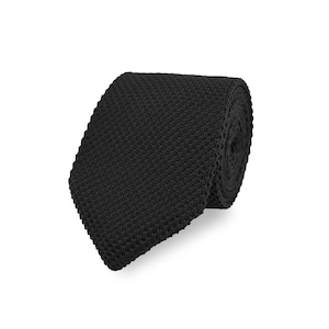 Könnte beinhalten: Eine einfarbige schwarze Krawatte mit einer ausgeprägten Strickstruktur und einem quadratischen Ende. Die Krawatte ist zu einer kompakten Rolle gewickelt, die das gleichmäßige Webmuster und die tiefe, einheitliche schwarze Farbe über die gesamte Länge zeigt.