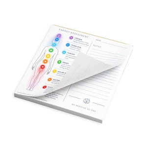 May include: A square notepad titled Energy Assessment featuring a human outline with seven colored chakra points. The page includes a list of chakras with descriptions, a date line, and a notes section. The bottom text reads We Breathe As One.