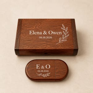 Puede incluir: Una caja rectangular de madera marrón oscuro y una memoria USB ovalada de madera a juego. La tapa de la caja presenta el texto grabado en blanco Elena & Owen, la fecha 06.18.2026 y una ramita. La memoria USB muestra E & O, 06.18.2026 y una ramita.
