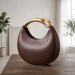 Borsa a mezzaluna realizzata a mano in pelle marrone cioccolato con manico scultoreo dorato.