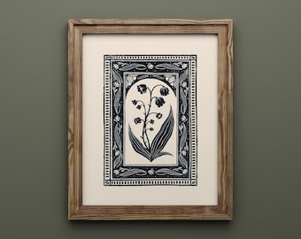 May include: A framed art print featuring a dark blue linocut illustration of a lily of the valley plant centered within an arched frame. The design is surrounded by a rectangular border with small floral motifs, all set on a cream background.