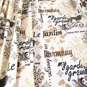 Könnte beinhalten: Weißer Stoff mit einem sich wiederholenden Muster aus Blumen- und Vogelmotiven sowie den Phrasen "Le Jardin", "in the breeze" und "my garden grows". Das Design enthält braune, beige und schwarze Elemente.