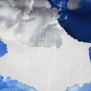 May include: Close-up of fabric with a watercolour design. The pattern features large, abstract shapes in shades of blue, grey, and white. The fabric has a textured appearance with vertical lines, creating a subtle striped effect.