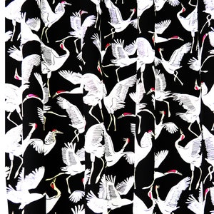 May include: Black fabric with a repeating pattern of white cranes in various poses. The cranes have red accents on their heads and legs. The design is a classic, elegant style, suitable for apparel or home decor.