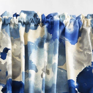 May include: A valance curtain with a watercolour-style pattern in shades of blue, grey, and white. The fabric is gathered at the top, and the ends are held by decorative wooden finials.