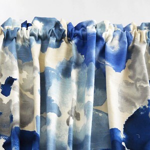 May include: A valance curtain with a watercolour-style pattern in shades of blue, grey, and white. The fabric is gathered at the top, and the ends are held by decorative wooden finials.