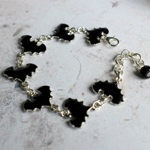 May include: A silver chain bracelet with black bat charms and a black bead. The bracelet has a lobster clasp closure.
