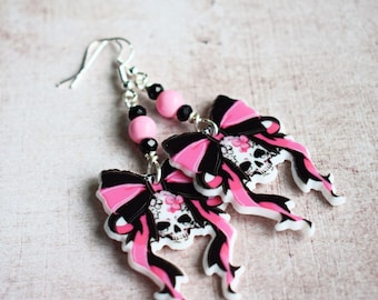 May include: Pink and black skull earrings with a bow design. The earrings are made of polymer clay and have silver hooks.